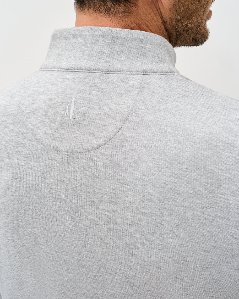 Close-up of a person wearing a gray pullover with a brand logo on a white background