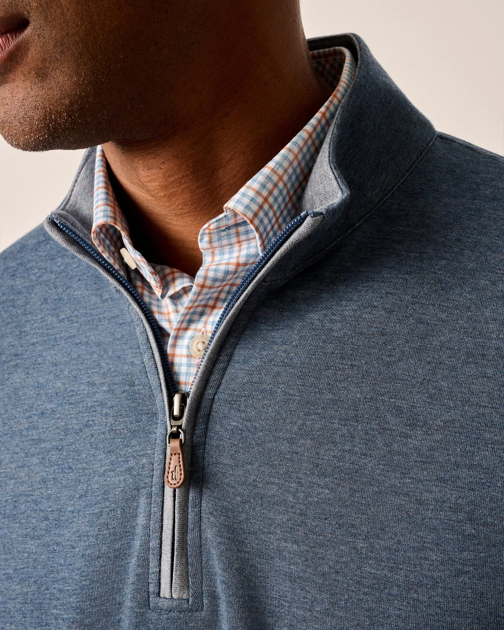 Close-up of a person wearing a blue half-zip sweater over a plaid shirt.